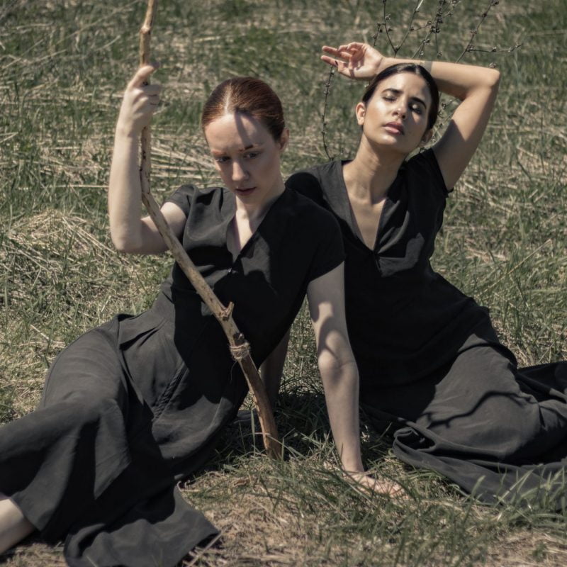 Two women in a field wearing black organic dresses