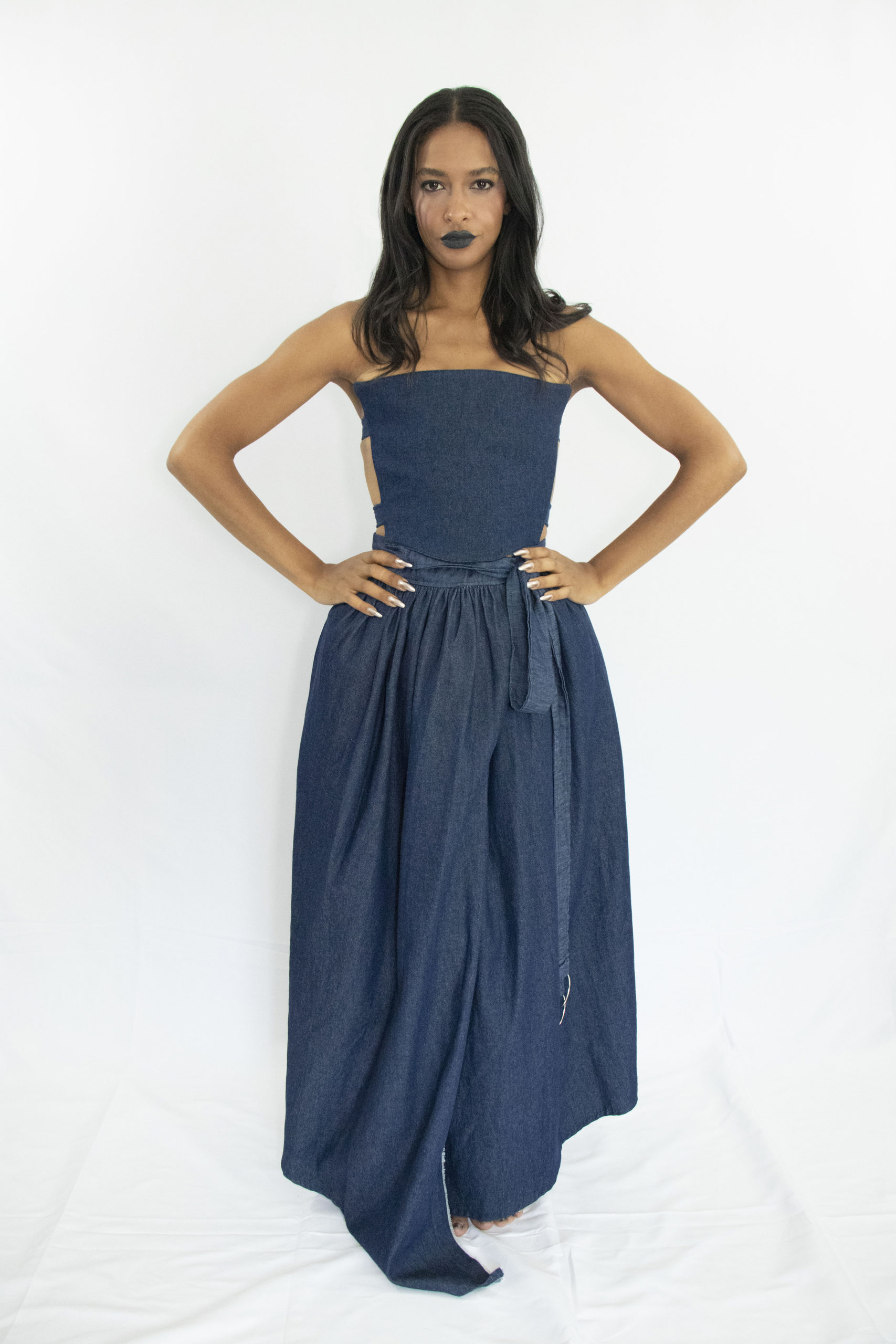 Woman wearing dark blue denim wrap assymetrical skirt with side pockets and oversized belt closure at the waist