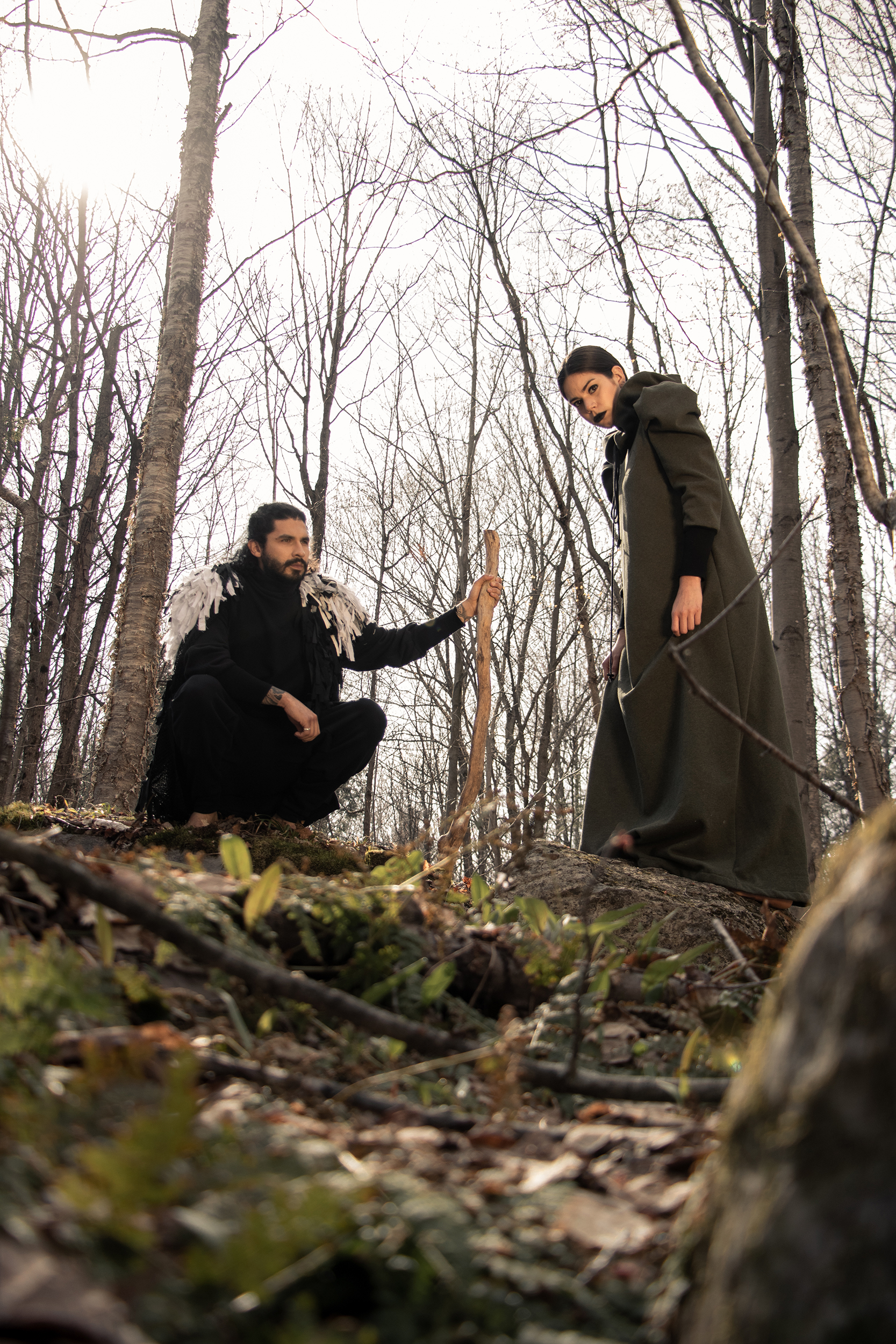 Man wearing sustainable organic cotton black tracksuit with zero waste fringed cape and woman wearing organic cotton green dress in the woods