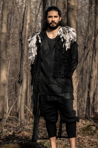 Man wearing black tunic with black organic sweatpants and a zero waste black and white fringed cape in the woods