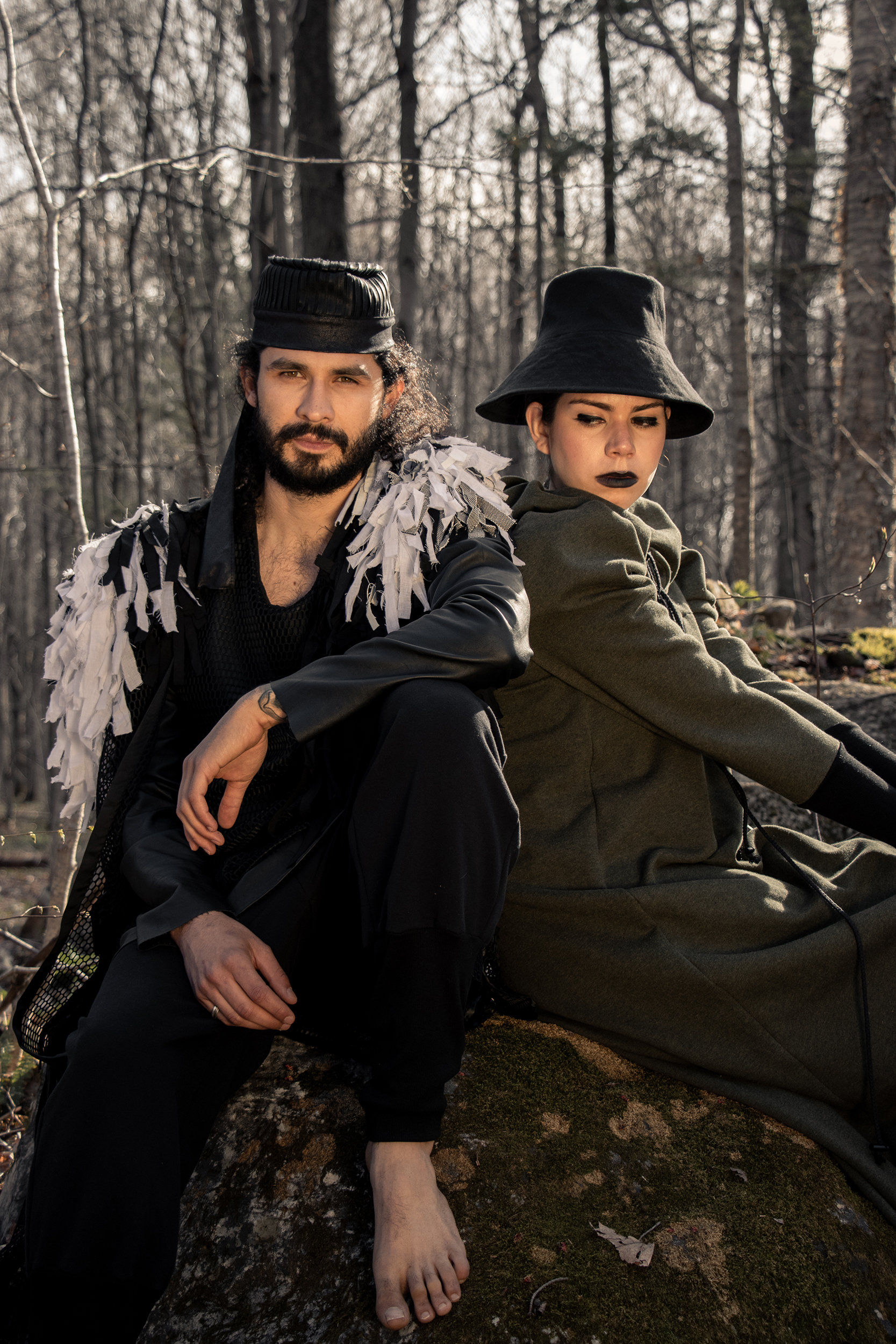 Man wearing sustainable organic cotton black tracksuit with zero waste fringed cape and woman wearing organic cotton green dress in the woods