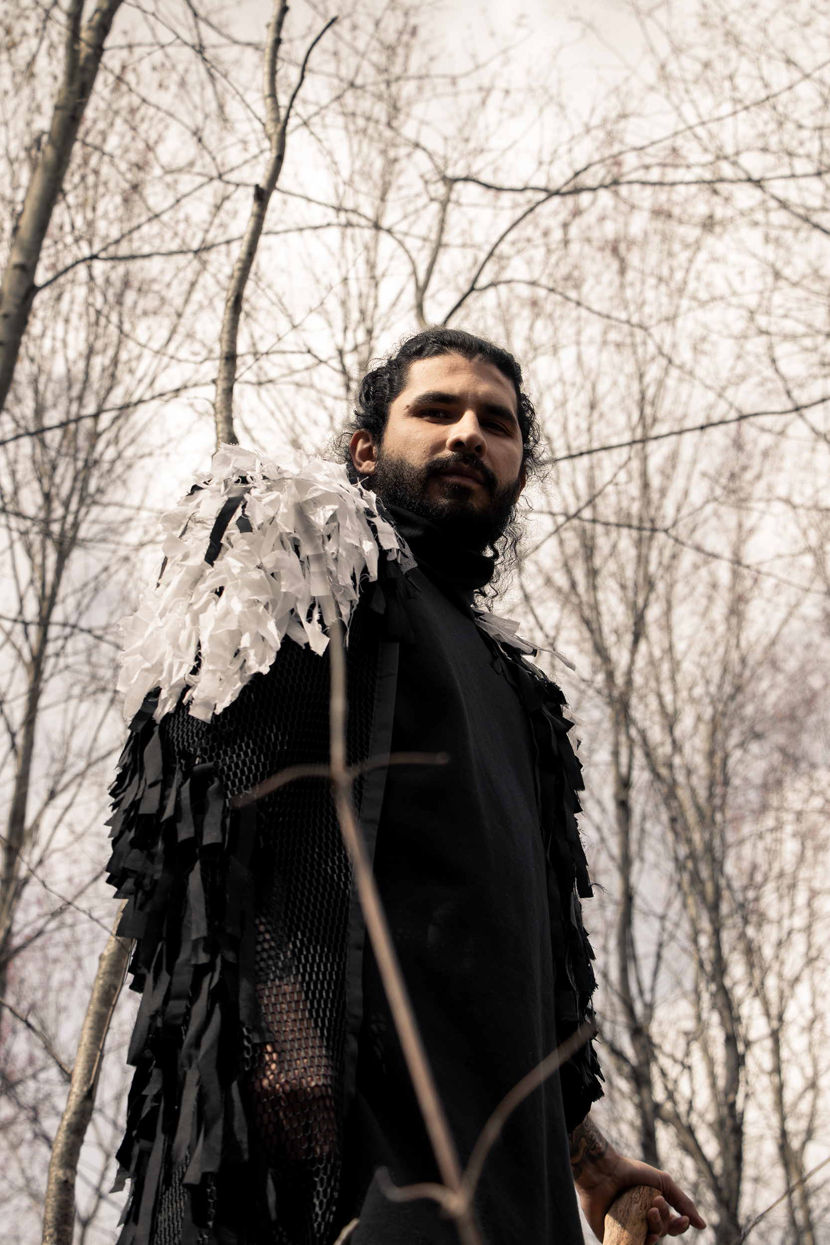 Man wearing sustainable organic cotton black tracksuit with zero waste fringed cape in the woods
