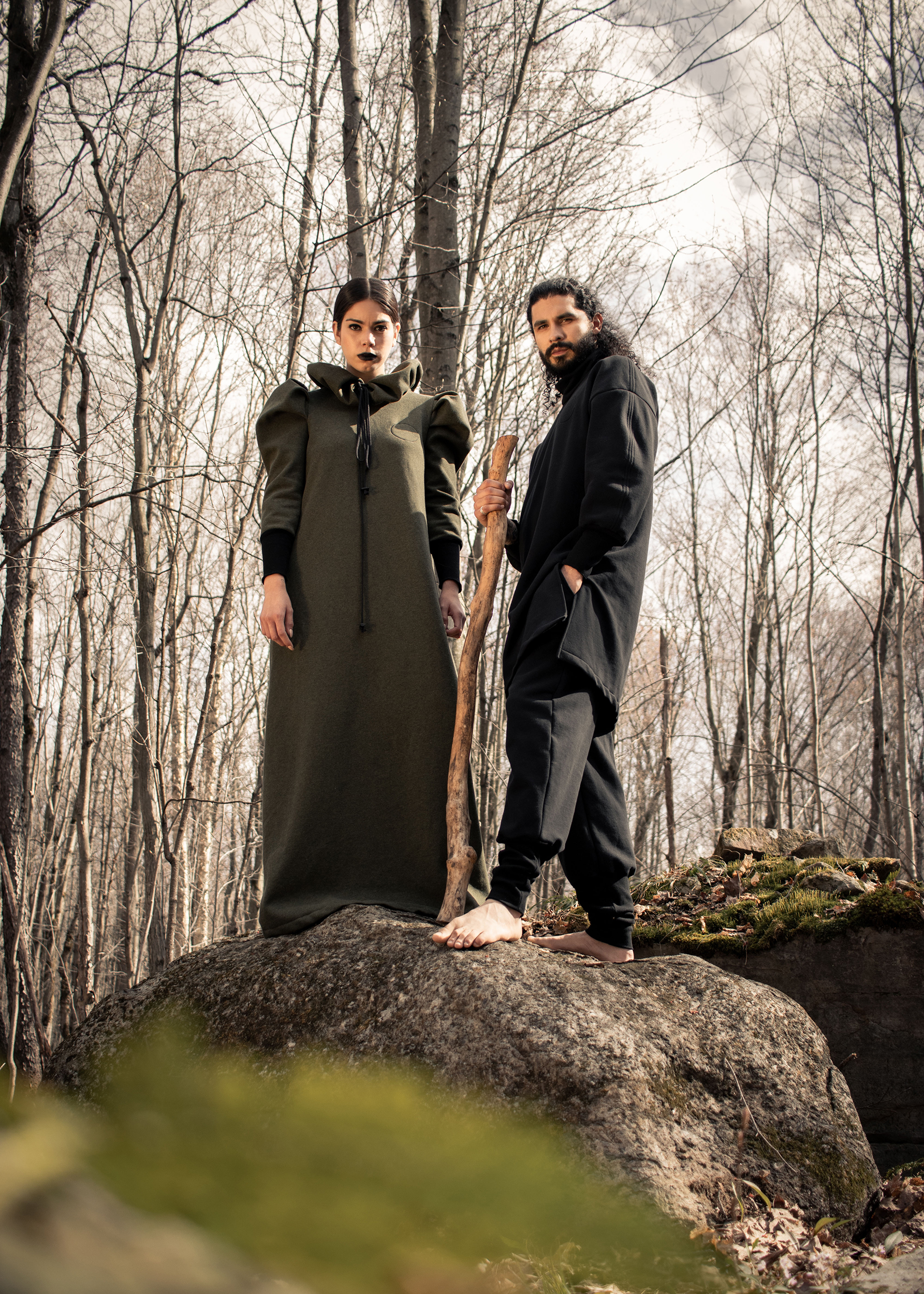 Man wearing sustainable organic cotton black tracksuit and woman wearing organic cotton green dress in the woods
