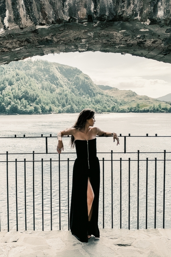 Woman wearing long black dress with open front slit in a lakefront castle